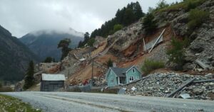 A dreary landscape of a landslide aftermath in a mountainous region, depicting debris and damaged homes, muted colors.